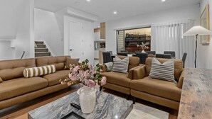 A modern living room with a brown sofa set, a marble coffee table, and a vase of flowers. - ﻿Premium Sunset Townhouse | 6 Aircons near Airport (Auckland South)