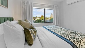 A hotel room with a bed, a window with curtains, and a view of the outside. - ﻿Premium Sunset Townhouse | 6 Aircons near Airport (Auckland South)