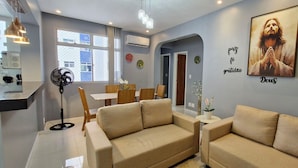 Ein modernes Wohnzimmer mit beigefarbenen Sofas, einem Essbereich mit Holzmöbeln und einer Wand mit motivierenden Texten und einem gerahmten Bild.