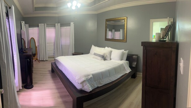 A bedroom with a large bed, a wooden headboard, a bedside table, a mirror, and a wardrobe. - Newly renovated, spacious, modern home near Hospitals and LSU. (Baton Rouge)