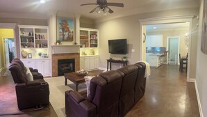 A spacious living room with a fireplace, leather sofas, a flat-screen TV, and a bookshelf. - Newly renovated, spacious, modern home near Hospitals and LSU. (Baton Rouge)