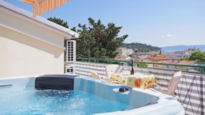 A rooftop terrace with a hot tub, outdoor seating, and a view of a town and hills. - Apartments Ribarević (Makarska)