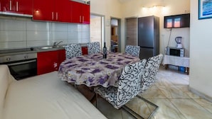 A compact kitchen with red cabinets, a built-in oven, and a dining area with a patterned tablecloth. - Apartments Ribarević (Makarska)
