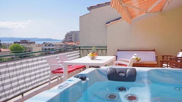 A balcony with a hot tub, outdoor seating, and a view of the cityscape. - Apartments Ribarević (Makarska)