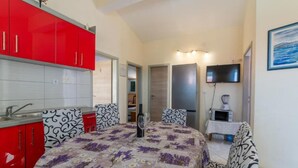 A compact hotel room with a kitchenette, a bed with floral bedding, and a TV on the wall. - Apartments Ribarević (Makarska)