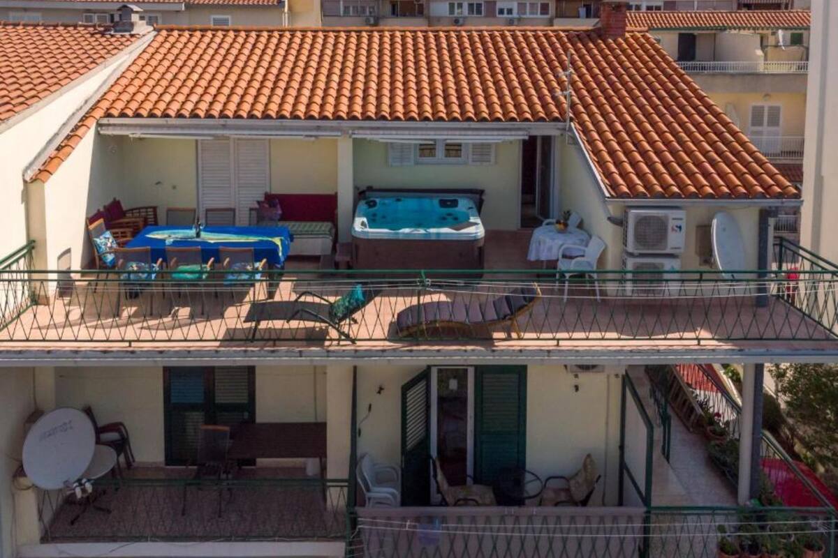 A two-story building with a tiled roof, outdoor seating area with tables and chairs, and a hot tub.