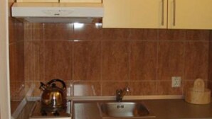 A kitchen with beige cabinets, a stainless steel sink, and a kettle on the counter. - Apartments Krvavac (Slivno)