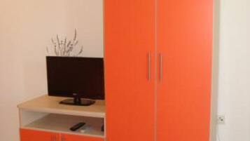 Una habitación con un armario anaranjado grande, un televisor de pantalla plana sobre un mueble bajo y una planta pequeña en el suelo.