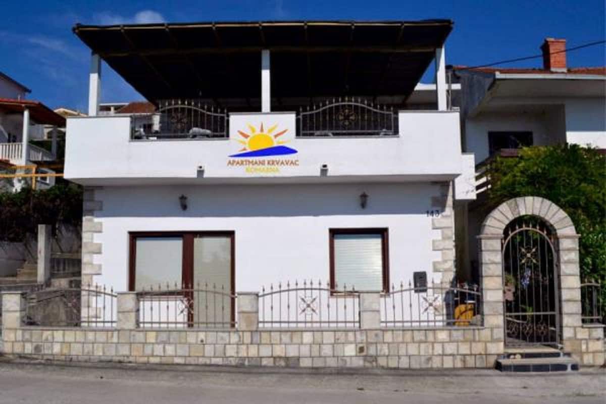 A two-story building with a sign reading "APARTMANI KRIVAC" and a sun symbol.