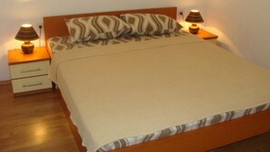 A neatly made bed with a patterned pillow and a beige blanket, flanked by two bedside tables with lamps. - Apartments Krvavac (Slivno)