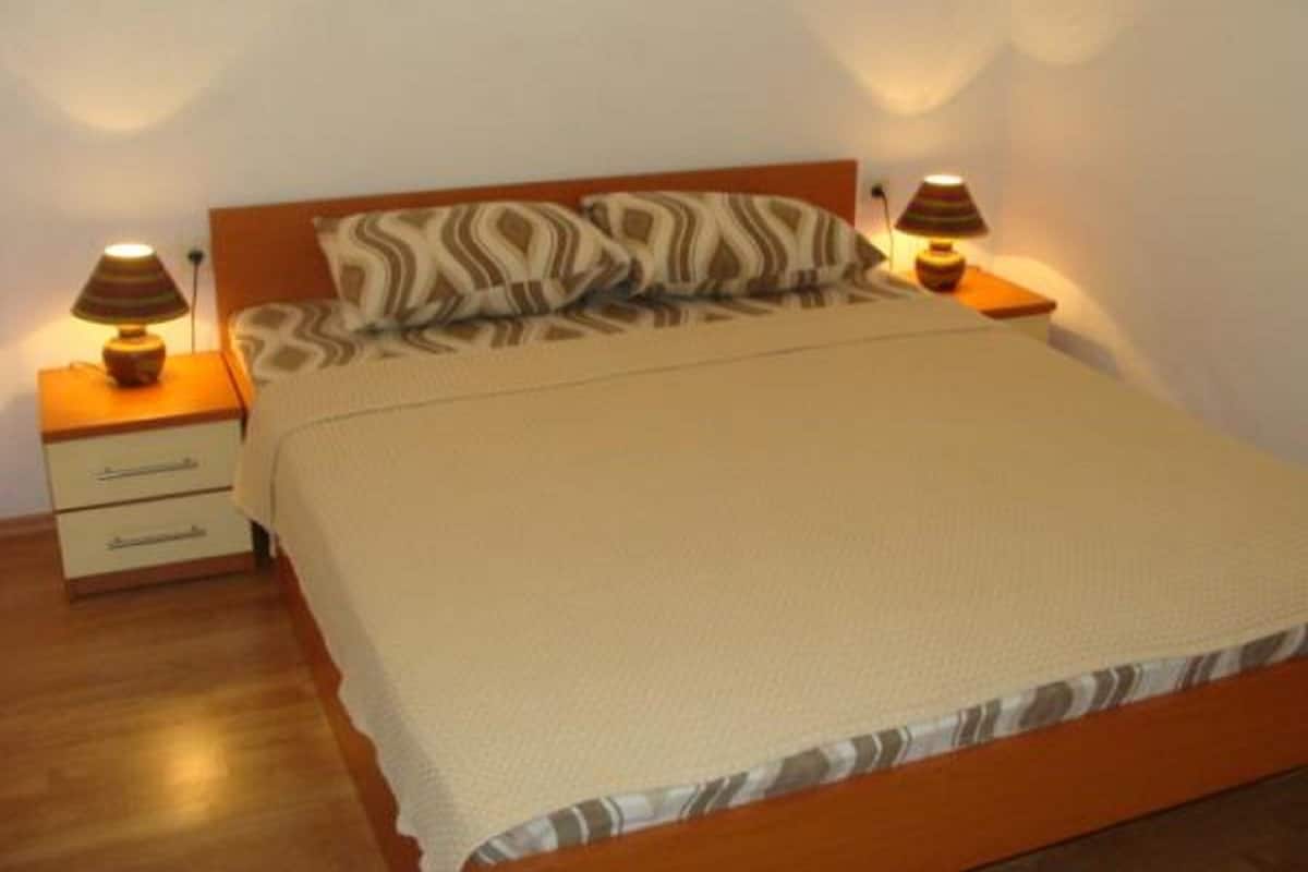 A neatly made bed with a patterned pillow and a beige blanket, flanked by two bedside tables with lamps.