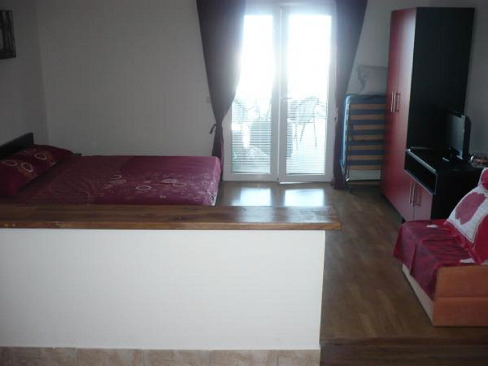 Un dormitorio con una cama, un banco de madera, un sofá rojo y un televisor.