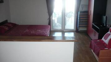 Un dormitorio con una cama, un banco de madera, un sofá rojo y un televisor.