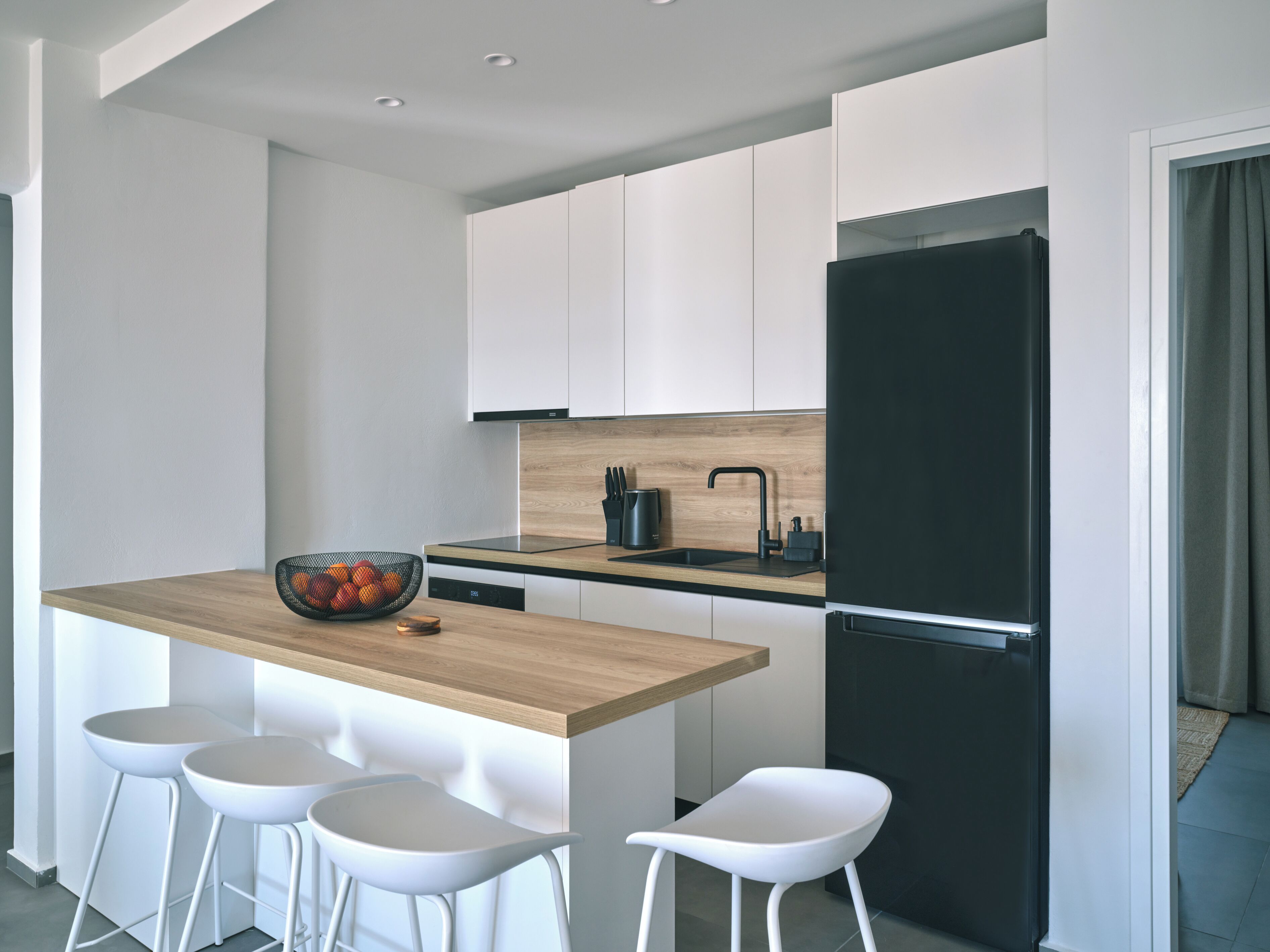 A modern kitchen with a wooden island, white bar stools, a black refrigerator, and white cabinets.