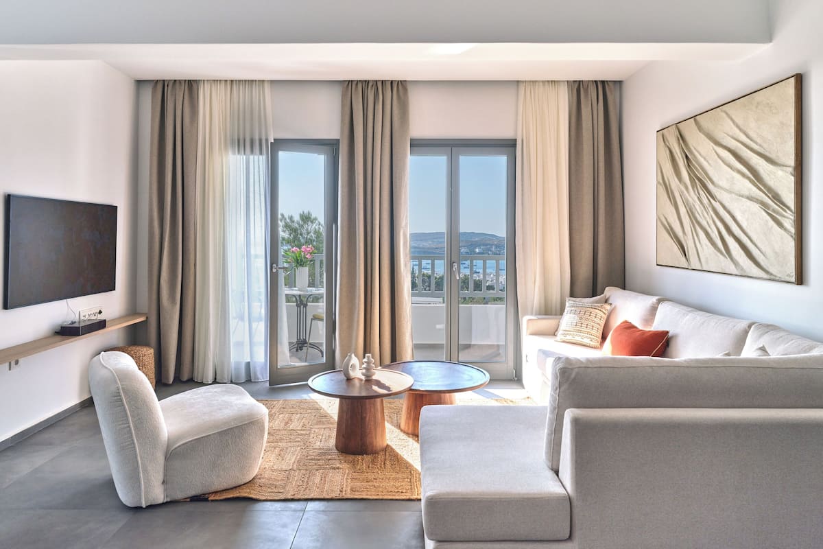 A modern living room with a flat-screen TV, a sofa, a coffee table, and a balcony with curtains.