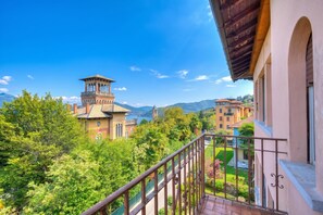 A balcony with a view of a building with a tower, lush greenery, and mountains in the background. - Lorenza Rooftop: Lake Maggiore View Balcony near Stresa, Stresa, Italy (Stresa)