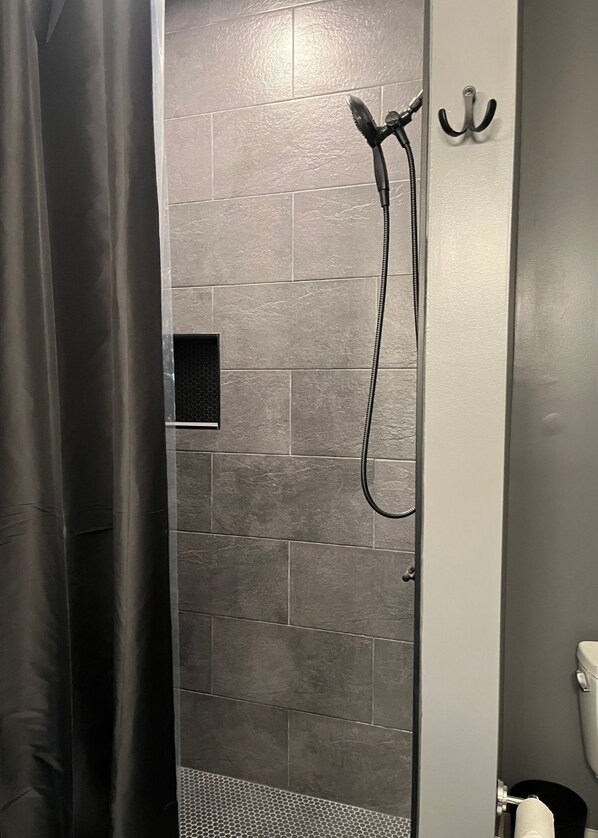 A shower area with a tiled wall, a showerhead, and a towel rack.