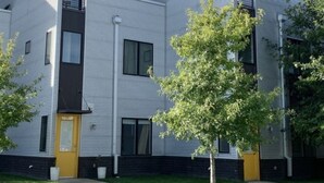 Un immeuble résidentiel moderne à plusieurs étages, doté d’un toit plat, de grandes fenêtres et d’une porte jaune.