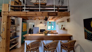 Une cuisine rustique avec un îlot central en bois, deux chaises en osier et une maquette de bateau sur l’étagère supérieure.