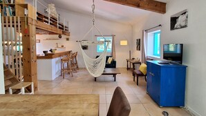 Un grand espace de vie comprenant un escalier en bois, un hamac, une table à manger et un téléviseur.