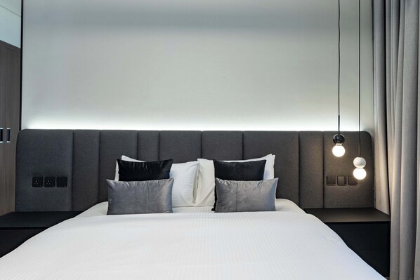 A modern bedroom with a large bed, grey upholstered headboard, and bedside lamps.