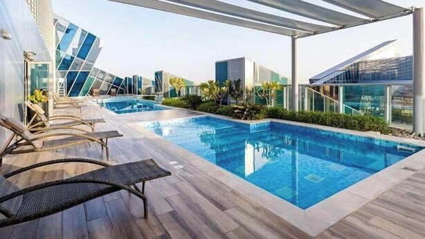 A rooftop swimming pool with lounge chairs and a glass building in the background. - 1 BR in J One Tower 5 minutes from Dubai Mall (Dubai)