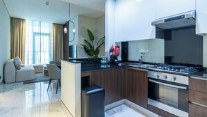 A modern kitchen with a gas stove, oven, and a built-in island. There is a seating area with a sofa and chairs. - 1 BR in J One Tower 5 minutes from Dubai Mall (Dubai)