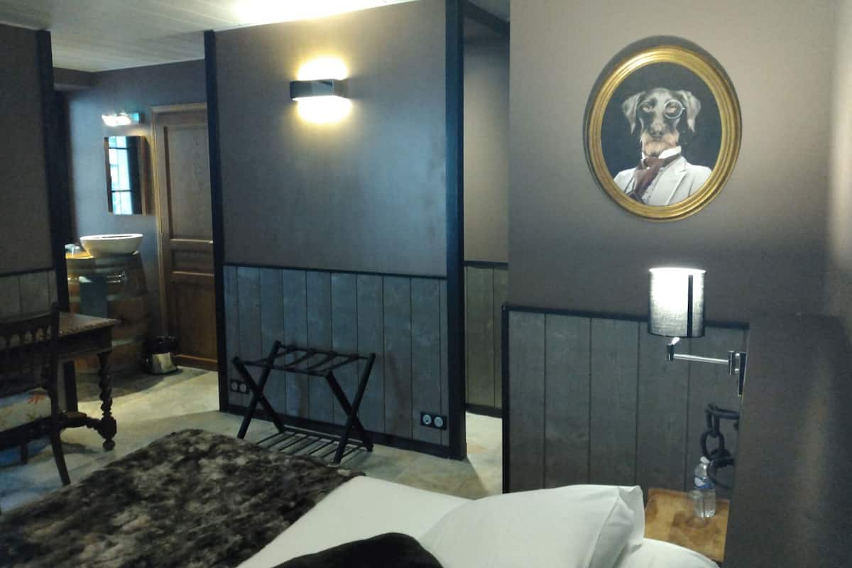 A hotel room with a bed, a small table, a chair, a wall-mounted picture, and a wall-mounted light fixture.