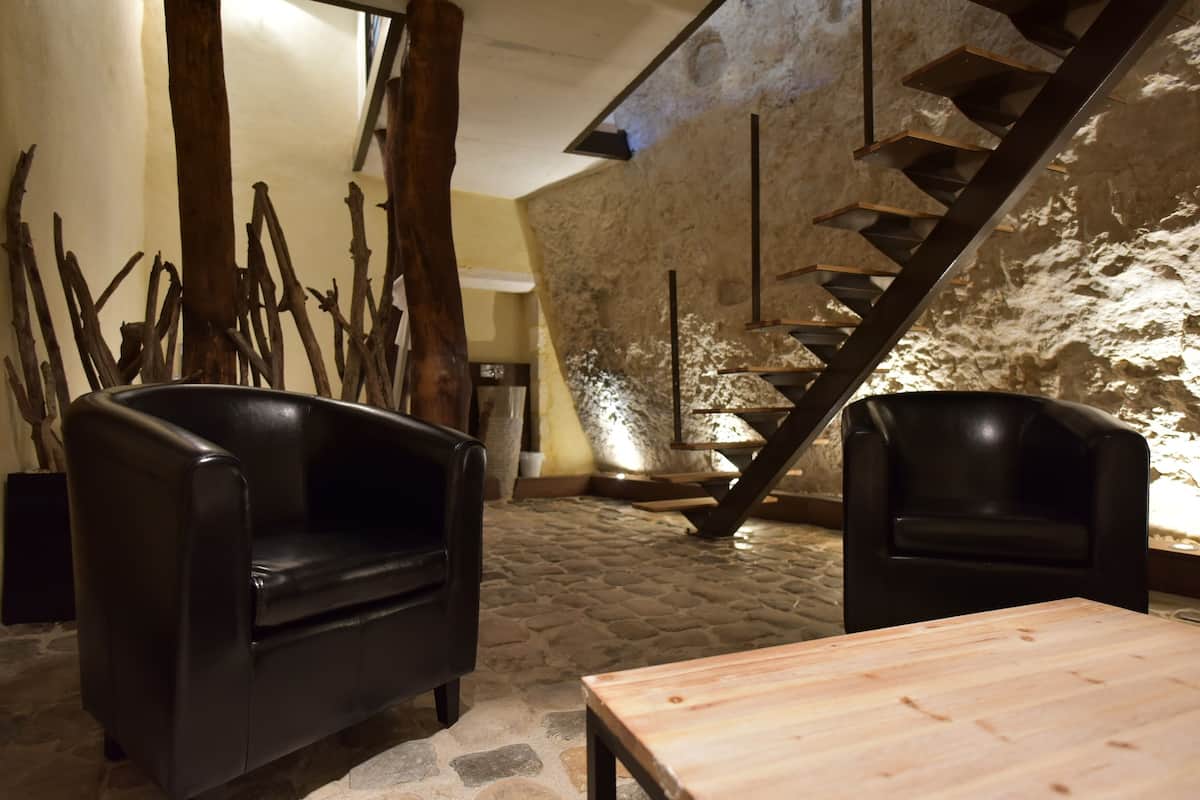 A cozy interior with a stone wall, a wooden staircase, and two black leather chairs.