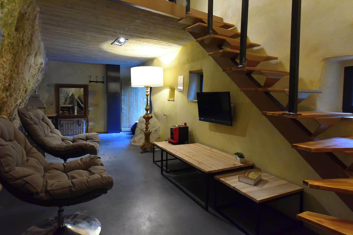 A modern interior with a sofa, a wooden table, a lamp, a TV, and a staircase.
