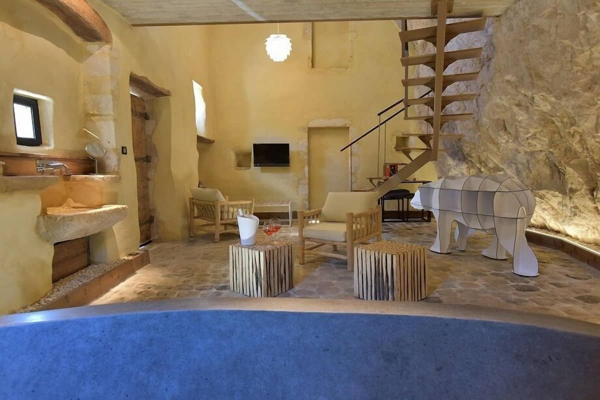 A rustic interior with stone walls, wooden furniture, a stone sink, and a staircase.