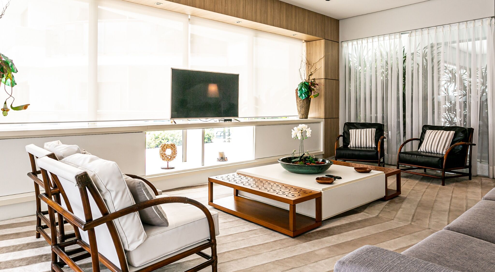 Uma sala de estar moderna com um sofá, poltronas, uma mesa de centro e uma televisão.