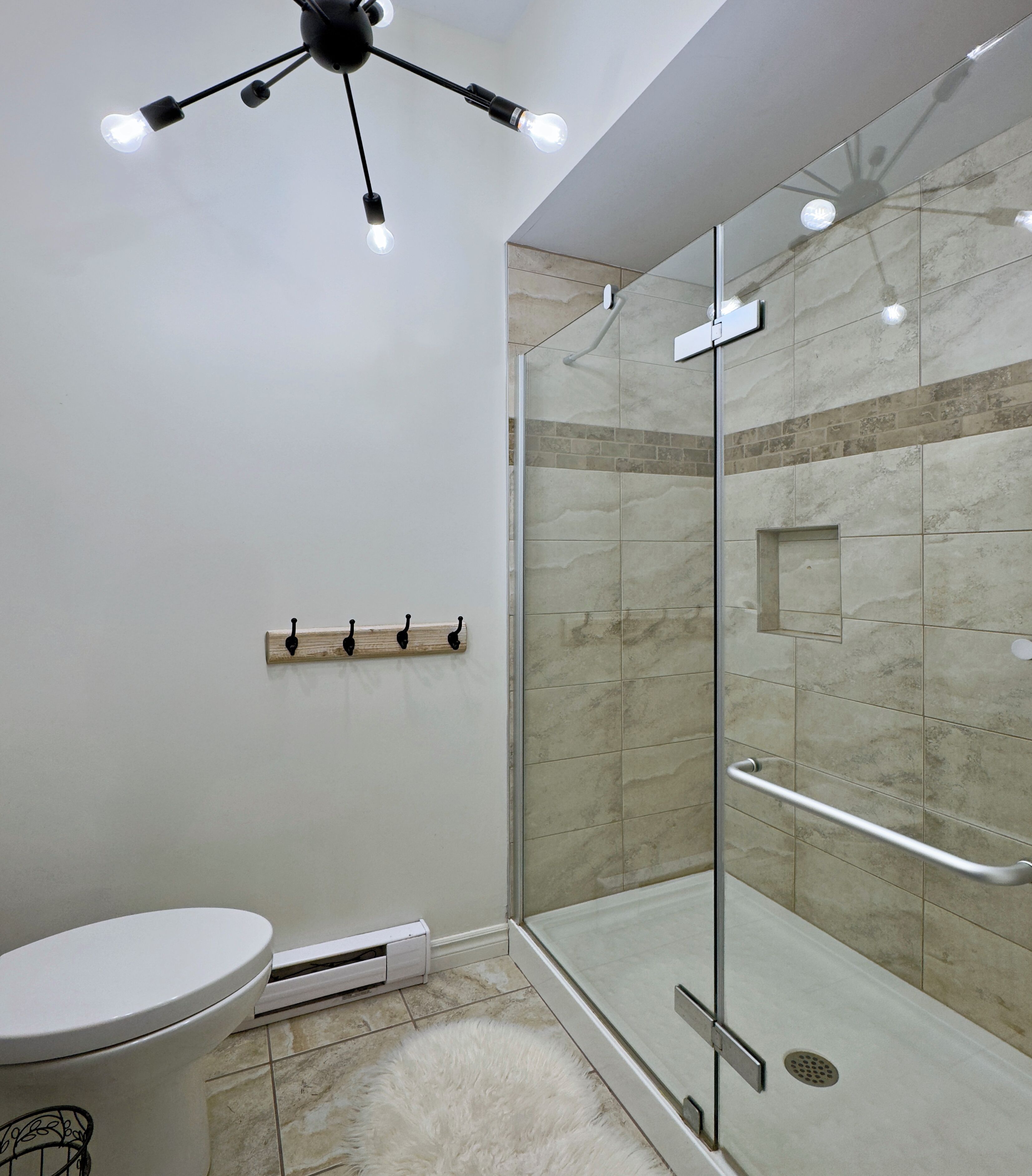 Een moderne badkamer met een douchecabine van glas, een wit toilet en een plafondlamp.