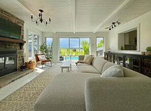 A spacious living room with a fireplace, a large sofa, and a view of a swimming pool.