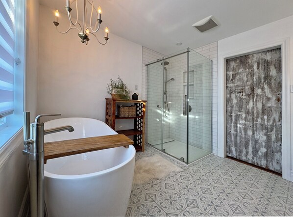 A modern bathroom with a freestanding bathtub, a glass-enclosed shower, and a decorative chandelier.