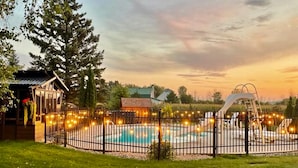 Un'area piscina con recinzione, un piccolo deposito e un albero grande.