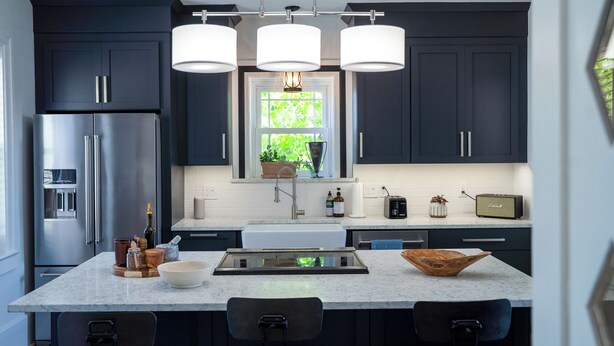 A modern kitchen with dark cabinetry, a stainless steel refrigerator, a large island with bar stools, and pendant lighting.