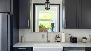 A modern kitchen with dark cabinets, a white sink, a window with a view of greenery, and a hanging lantern.