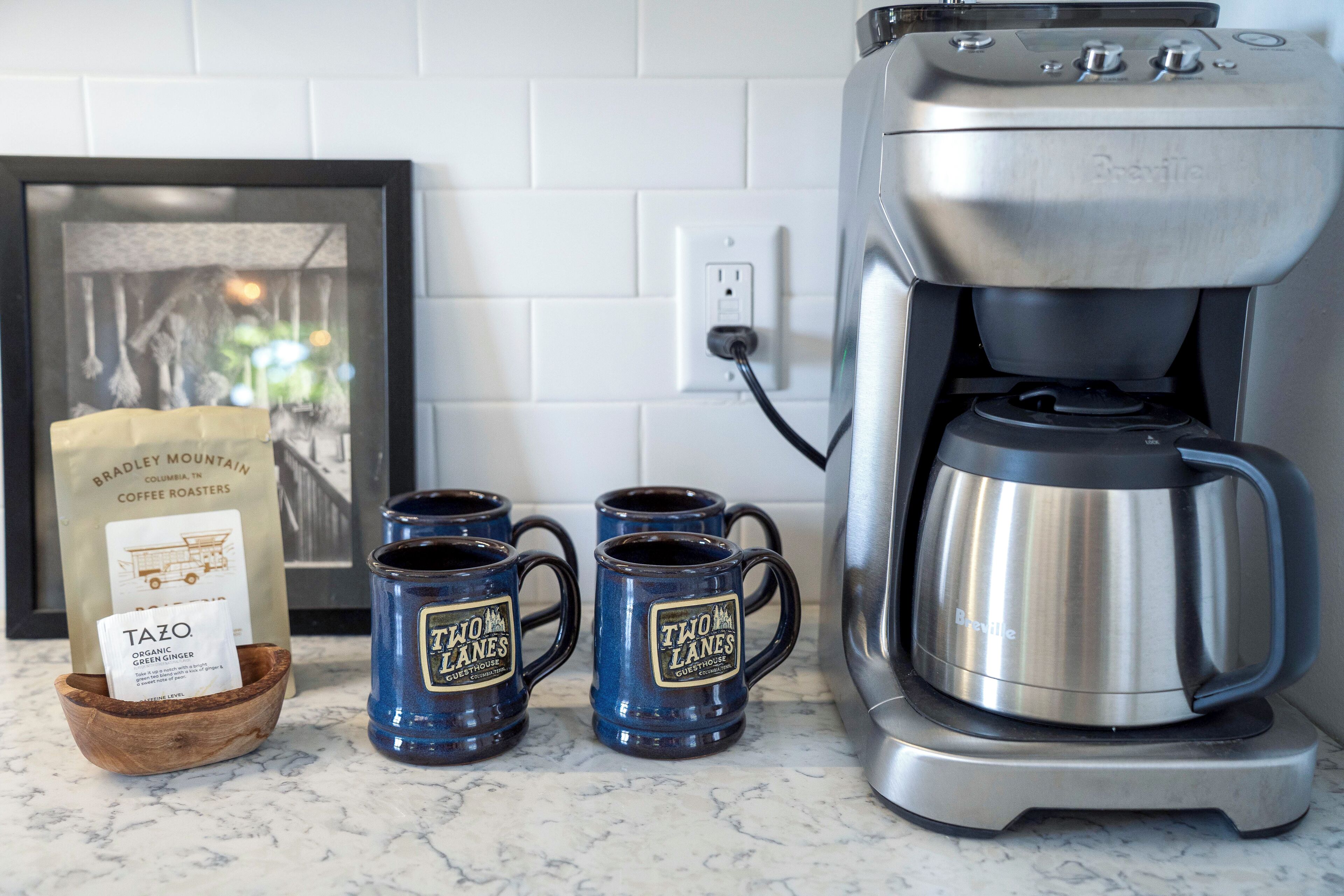 Una cafetera, dos tazas y un paquete de café sobre una encimera de cocina.