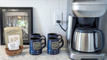 Una cafetera, dos tazas y un paquete de café sobre una encimera de cocina.