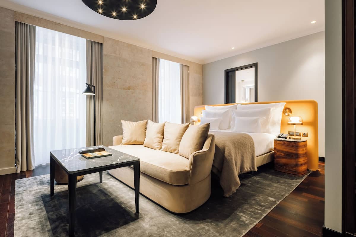 Una habitación de hotel moderna con sofá, una mesita, una lámpara de noche y una mesita de noche.