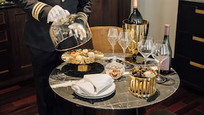 A table set with a bottle of champagne, wine glasses, a gold dessert plate, and a basket of grapes.