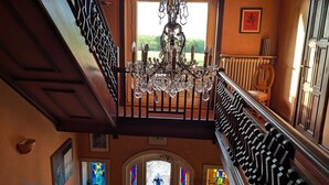 A grand staircase with ornate railings, a chandelier, and a view of the outdoors through a door with stained glass. - Auberge des Chasseurs (Echenevex)
