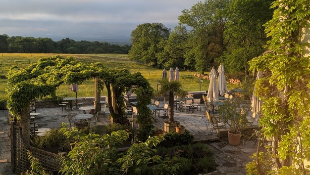 An outdoor patio area with stone flooring, surrounded by lush greenery and trees. - Auberge des Chasseurs (Echenevex)
