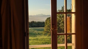 A room with a large window revealing a scenic view of a green landscape and distant mountains. - Auberge des Chasseurs (Echenevex)