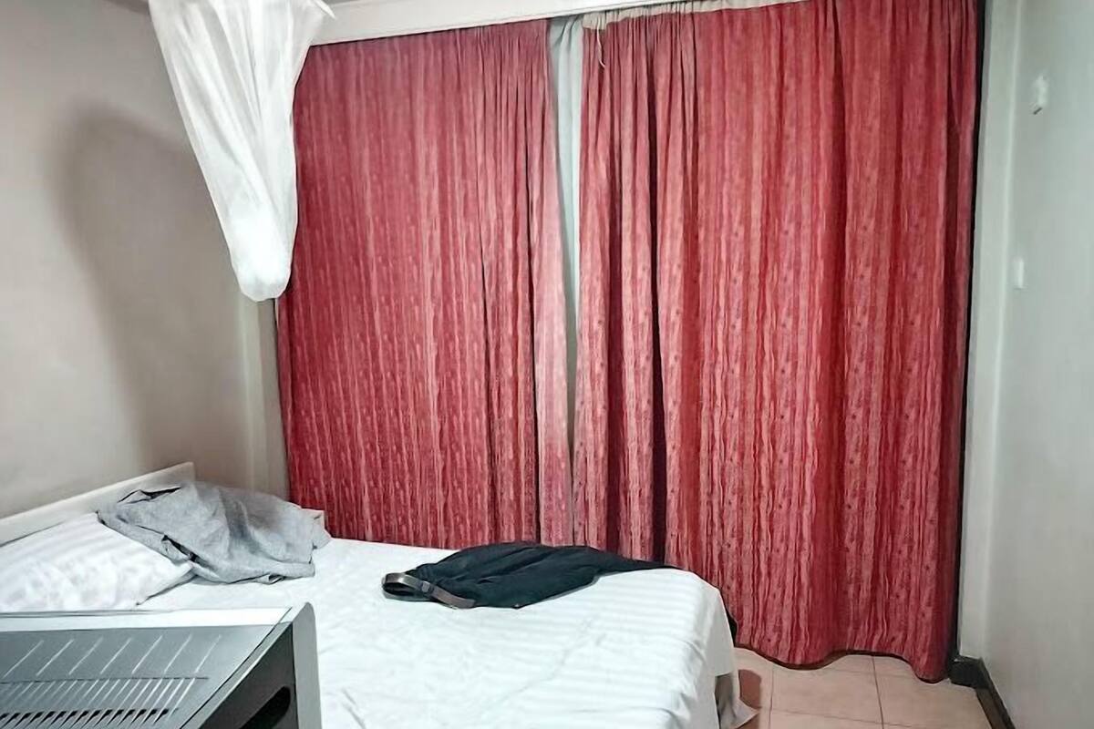 A bedroom with a bed, a desk, and a red curtain.