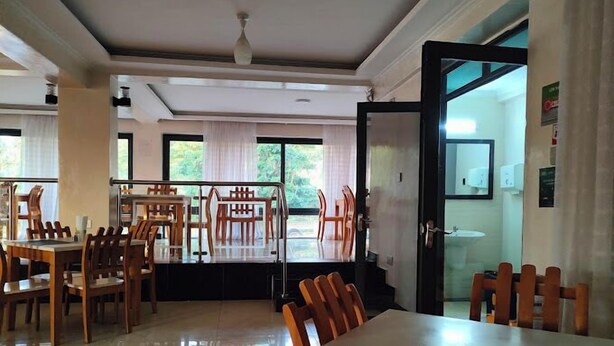 A spacious dining area with multiple tables and chairs, large windows with curtains, and a ceiling fan. - Hotel Twin Towers Homa Bay (Homa Bay)