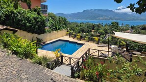 A pool area with a view of the sea, surrounded by lush greenery and a stone pathway leading to the pool. - Suítes Azul Marinho (Ilhabela)