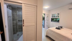 A bedroom with a bed, a shower area, and a door leading to a balcony. - Suítes Azul Marinho (Ilhabela)