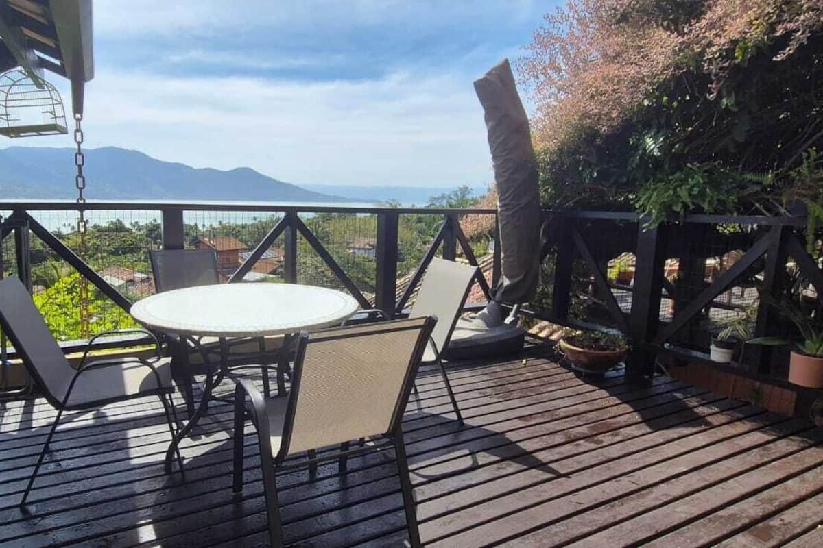 Eine Holzterrasse mit rundem Tisch und Stühlen, mit Blick auf eine gebirgige Landschaft.